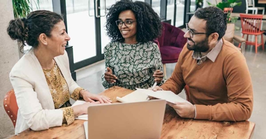 A man and woman smiling as they work with another woman. The man is holding paperwork, and both he and his wife are smiling at the other woman.