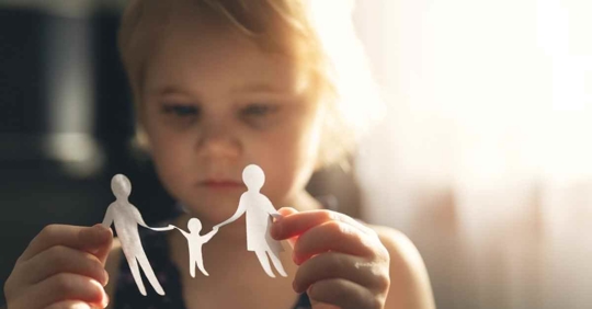 A young girl holding paper figures of two larger people and one smaller person in the middle