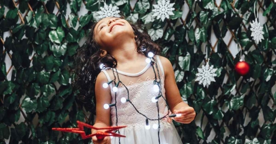A young girl playing with holiday lights and a star with large plastic snowflakes hanging around her